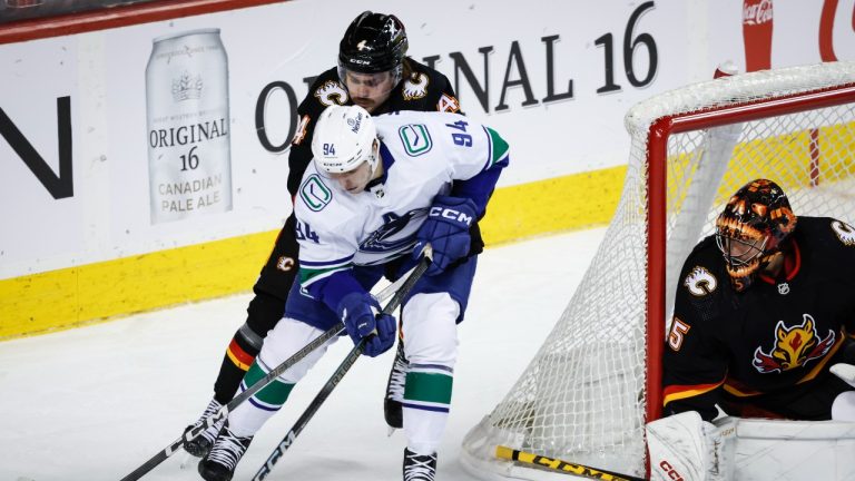 Vancouver Canucks forward Linus Karlsson, left, is checked by Calgary Flames defenceman Rasmus Andersson, centre, as goalie Jacob Markstrom looks on during second period NHL hockey action in Calgary, Thursday, Nov. 16, 2023. (Jeff McIntosh/THE CANADIAN PRESS)