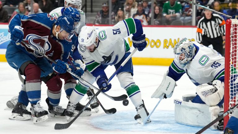 Colorado Avalanche center Andrew Cogliano, left, shoots the puck past Vancouver Canucks defenseman Mark Friedman, center, at goaltender Thatcher Demko during the first period of an NHL hockey game Wednesday, Nov. 22, 2023, in Denver. (David Zalubowski/AP)