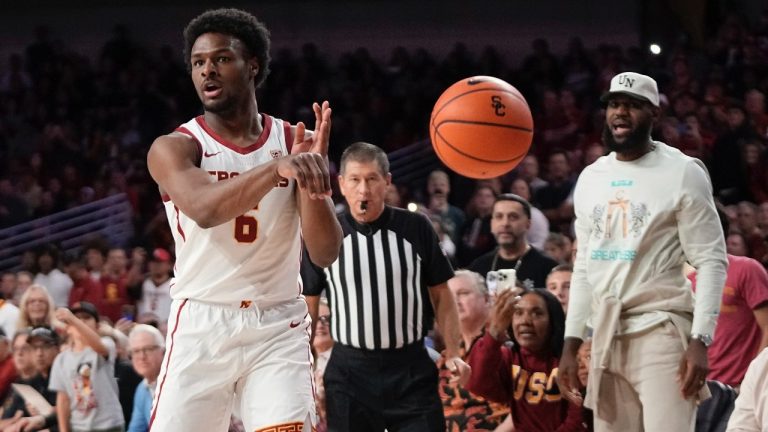 Southern California guard Bronny James, left, passes the ball as his father LeBron James, right, watches during the first half of an NCAA college basketball game against Long Beach State Sunday, Dec. 10, 2023, in Los Angeles. (AP Photo/Mark J. Terrill)