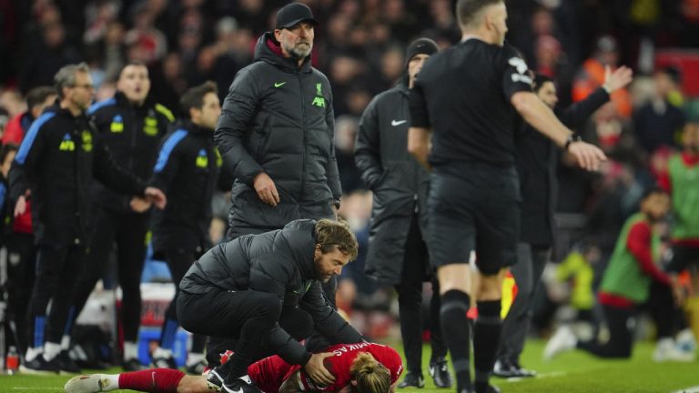 Liverpool's Kostas Tsimikas, bottom, grimaces in pain after a tackle by Arsenal's Bukayo Saka during the English Premier League soccer match between Liverpool and Arsenal at Anfield stadium in Liverpool, England, Saturday, Dec. 23, 2023. (Jon Super/AP)