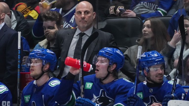 Vancouver Canucks head coach Rick Tocchet, back, stands on the bench behind Elias Pettersson, front from left to right, Brock Boeser and Conor Garland during the third period of an NHL hockey game against the Calgary Flames in Vancouver, on Saturday, March 23, 2024. (Darryl Dyck/CP)