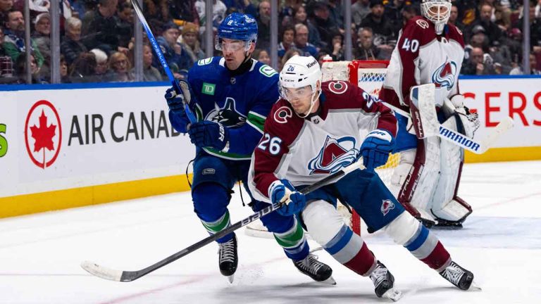 Vancouver Canucks' Conor Garland (8) and Colorado Avalanche's Sean Walker (26) vie for the puck as goaltender Alexandar Georgiev (40) watches during the first period of an NHL game. (Ethan Cairns/CP)