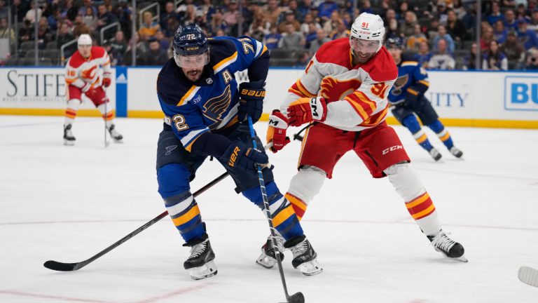 St. Louis Blues' Justin Faulk (72) reaches for a loose puck as Calgary Flames' Nazem Kadri (91) defends during the first period of an NHL hockey game Thursday, March 28, 2024, in St. Louis. (Jeff Roberson/AP)