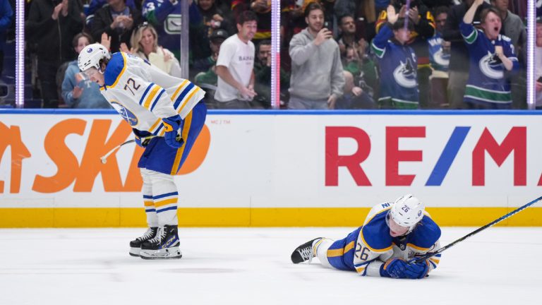 Buffalo Sabres' Rasmus Dahlin (26) lies on the ice as Tage Thompson (72) looks on while fans celebrate after Vancouver Canucks' Elias Pettersson, not seen, scored into the empty net to record his second goal, during the third period of an NHL hockey game in Vancouver, on Tuesday, March 19, 2024. (Darryl Dyck/CP)