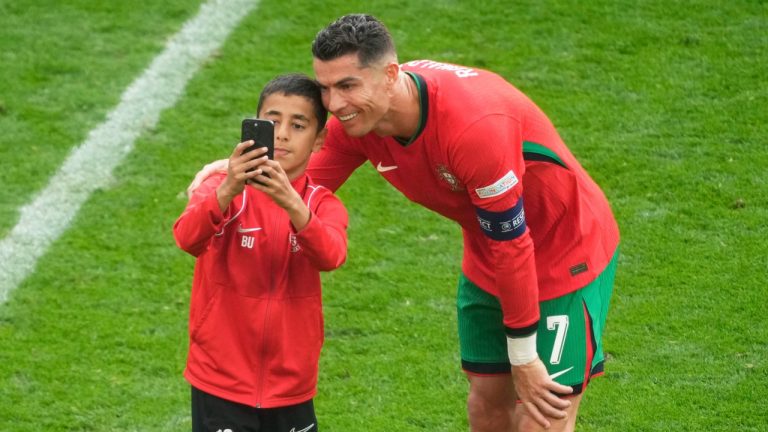 A young pitch invader takes a selfie with Cristiano Ronaldo during match between Turkey and Portugal at Euro 2024 tournament, June 22, 2024. (AP Photo/Michael Probst)