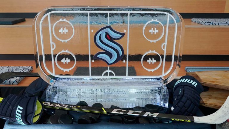 An ice sculpture of a hockey rink with the Seattle Kraken logo on it is displayed next to hockey gear Thursday, Sept. 9, 2021, during a media event for the opening of the Kraken's NHL hockey practice and community facility in Seattle. (Ted S. Warren/AP)