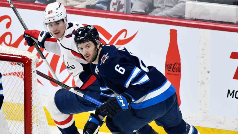 Winnipeg Jets' Colin Miller (6) skates behind goaltender Connor Hellebuyck (37) defending against Washington Capitals' Nicolas Aube-Kubel (96) during the first period of NHL action in Winnipeg on Monday March 11, 2024. (Fred Greenslade/CP)