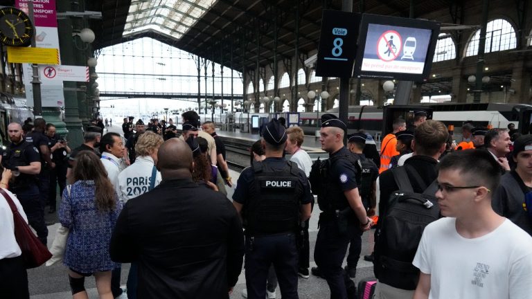 Travellers wait as police officers patrol inside the Gare du Nord train station at the 2024 Summer Olympics, Friday, July 26, 2024, in Paris, France. Hours away from the grand opening ceremony of the Olympics, high-speed rail traffic to the French capital was severely disrupted on Friday by what officials described as "criminal actions" and sabotage. (Mark Baker/AP Photo)