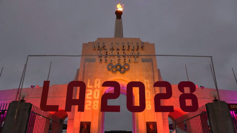 FILE - In this Sept. 13, 2017, file photo, an LA 2028 sign is seen in front of a blazing Olympic cauldron at the Los Angeles Memorial Coliseum. (Richard Vogel/AP) 