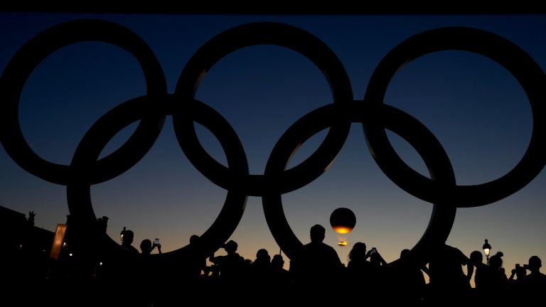 People watch the cauldron rise at sunset by the Olympic rings during the 2024 Summer Olympics, Monday, Aug. 5, 2024, in Paris, France. (Natacha Pisarenko/AP)