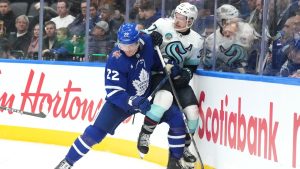 Seattle Kraken's Yanni Gourde is held up against the boards by Toronto Maple Leafs' Jake McCabe. (Chris Young/CP)