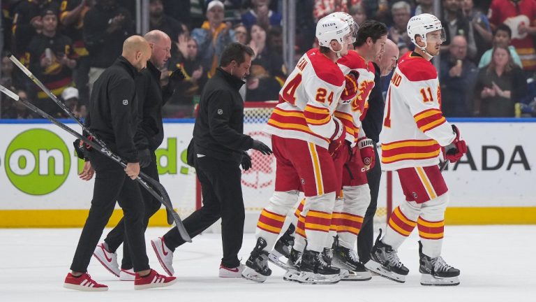 Calgary Flames' Kevin Rooney, second right, is helped off the ice by Jake Bean (24) as Mikael Backlund (11) skates with them after Rooney was checked into the boards during the first period of an NHL hockey game against the Vancouver Canucks, in Vancouver, on Wednesday, October 9, 2024. (Darryl Dyck/CP)