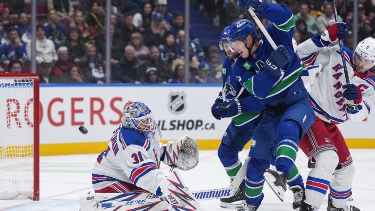 New York Rangers goalie Igor Shesterkin (31) makes the save as Vancouver Canucks' Aatu Raty, second right, watches while being checked by New York's Jacob Trouba (8) during first period NHL hockey action in Vancouver, B.C., Tuesday, Nov. 19, 2024. THE CANADIAN PRESS/Darryl Dyck