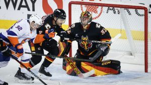 New York Islanders' Kyle MacLean, left, and Calgary Flames' Rasmus Andersson, centre, chase the puck in front of goalie Dustin Wolf during first period NHL hockey action in Calgary, Alta., Tuesday, Nov. 19, 2024. (Jeff McIntosh/CP)