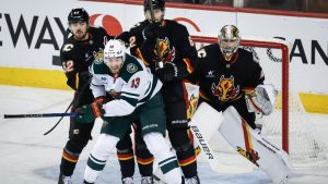 Minnesota Wild's Yakov Trenin (13) is checked by Calgary Flames MacKenzie Weegar (52) and Daniil Miromanov (62) as goalie Dustin Wolf looks on during first period NHL hockey action in Calgary on Saturday, Nov. 23, 2024. (Jeff McIntosh/CP)