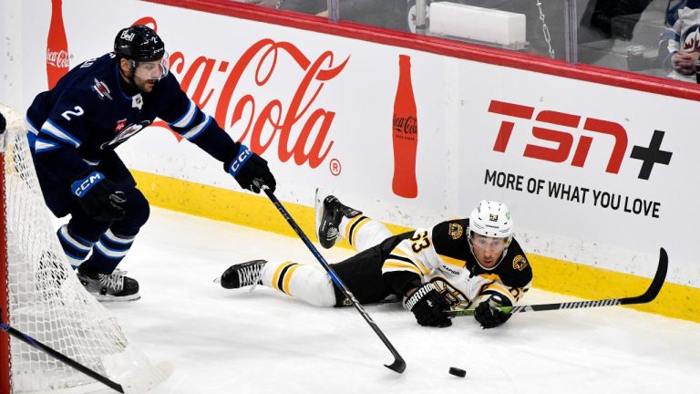 Boston Bruins' Brad Marchand (63) falls behind the net as Winnipeg Jets' Dylan Demelo (2) scoops up the loose puck during the first period, Tuesday December 10, 2024. (Fred Greenslade/CP)