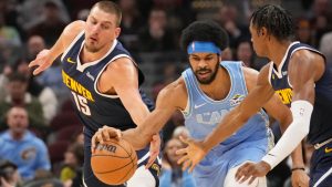 Denver Nuggets center Nikola Jokic (15), Cleveland Cavaliers center Jarrett Allen, center, and forward Peyton Watson, right, reach for the ball in the first half of an NBA basketball game, Thursday, Dec. 5, 2024, in Cleveland. (AP Photo/Sue Ogrocki)