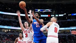 Philadelphia 76ers center Joel Embiid (21) drives to the basket against Chicago Bulls guard Josh Giddey (3) and center Nikola Vucevic (9) during the first half of an NBA basketball game in Chicago, Sunday, Dec. 8, 2024. (Nam Y. Huh/AP)