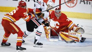 Chicago Blackhawks' Ilya Mikheyev, centre, tries to get the puck past Calgary Flames goalie Dustin Wolf, right, as Martin Pospisil checks during first period NHL hockey action in Calgary, Alta., Saturday, Dec. 21, 2024. (Jeff McIntosh/CP)