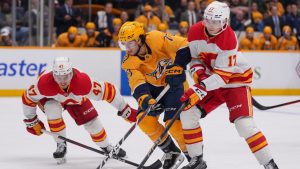 Nashville Predators right wing Luke Evangelista (77) skate the puck past Calgary Flames centre Connor Zary (47) and centre Yegor Sharangovich (17) during the second period of an NHL hockey game Tuesday, Dec. 10, 2024, in Nashville, Tenn. (George Walker IV/AP)