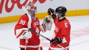 Canada goaltender Carter George and teammate Oliver Bonk (5) celebrates after defeating Germany in IIHF World Junior Hockey Championship tournament action in Ottawa, Sunday, Dec. 29, 2024. (Adrian Wyld/THE CANADIAN PRESS)