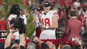 Ohio State quarterback Will Howard (18) holds a rose in his mouth as he poses with the trophy after the team won the quarterfinals of the Rose Bowl College Football Playoff against Oregon, Wednesday, Jan. 1, 2025, in Pasadena, Calif. (Mark J. Terrill/AP)