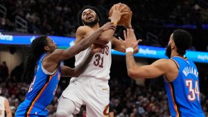 Cleveland Cavaliers center Jarrett Allen (31) is fouled by Oklahoma City Thunder guard Cason Wallace, left, as he drives to the basket between Wallace and Kenrich Williams (34), right, in the first half of an NBA basketball game, Wednesday, Jan. 8, 2025, in Cleveland. (Sue Ogrocki/AP)