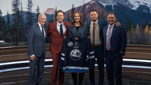 Ron MacLean, Elliotte Friedman, Jennifer Botterill, Kevin Bieksa and Kelly Hrudey pose with a Canmore Eagles sweater ahead of Hockey Day in Canada 2025.