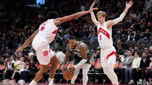 Milwaukee Bucks guard Damian Lillard (0) drives between Toronto Raptors forward Scottie Barnes (4) and teammate Gradey Dick (1) during second half NBA basketball action in Toronto, Monday, Jan. 6, 2025. (Nathan Denette/CP)