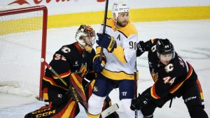 Nashville Predators' Ryan O'Reilly, centre, is checked by Joel Hanley, right, as goalie Dustin Wolf looks on Calgary Flames' during second period NHL hockey action in Calgary on Saturday, Jan. 4, 2025. (Jeff McIntosh/CP)