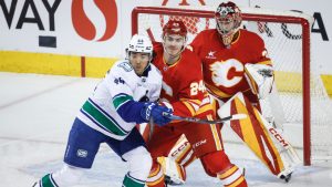 Vancouver Canucks' Kiefer Sherwood, left, and Calgary Flames' Jake Bean, centre, battle for position in front of goalie Dustin Wolf during first period NHL hockey action in Calgary, Alta., Wednesday, March 12, 2025. (Jeff McIntosh/CP)