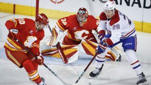 Montreal Canadiens' Christian Dvorak, right, and Calgary Flames' Jonathan Huberdeau, left, battle for the puck as goalie Dustin Wolf looks on during first period NHL hockey action in Calgary on Saturday, March 8, 2025. (Jeff McIntosh/CP)