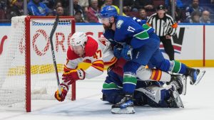 Calgary Flames' Connor Zary (47) celebrates his winning goal against Vancouver Canucks goalie Arturs Silovs, back, while being checked by Filip Hronek (17) during overtime NHL hockey action, in Vancouver, on Wednesday, October 9, 2024. (Darryl Dyck/CP)